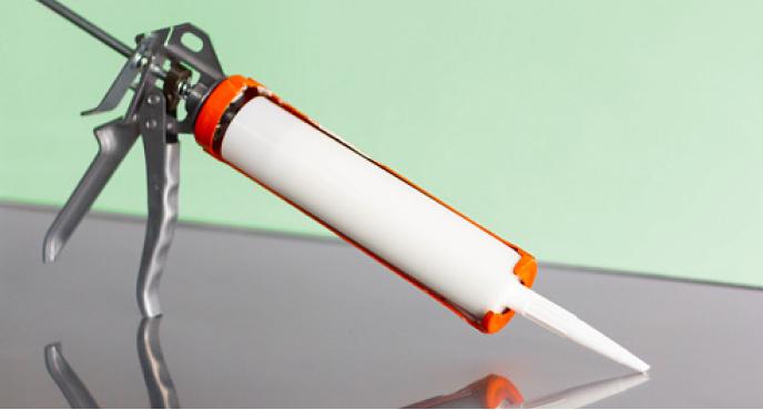 A caulk gun against a green background.
