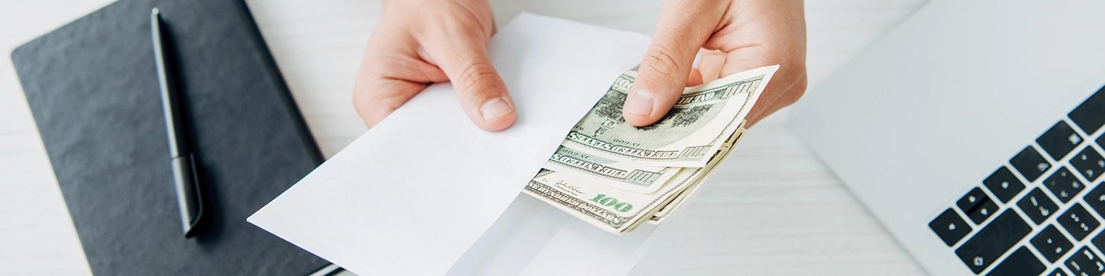 Hands Holding Money Next to a Laptop